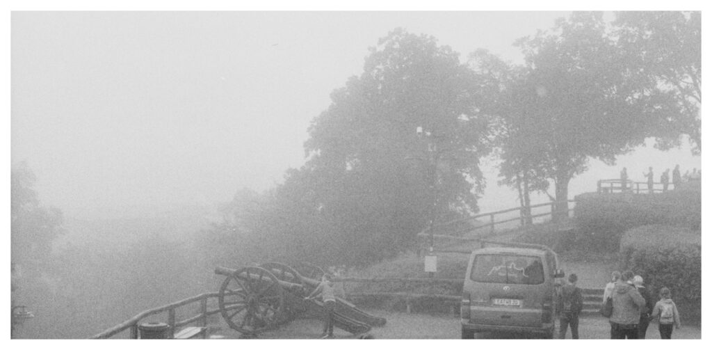a foggy view of an overlook, there are trees and people obscured by haze to the right. a cannon points out over a barely visible field
